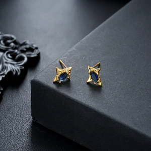 Macro shot of gold star-shaped earrings with blue marquise zircon and beaded edges