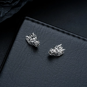 Macro view of vintage silver dragon head earrings on black leather texture background