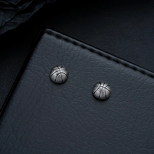 Detailed view of silver basketball earrings with textured finish on black leather surface