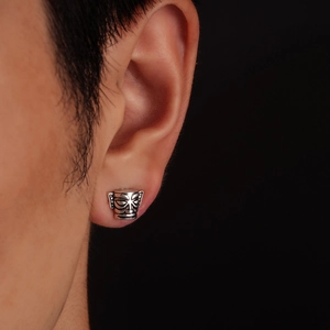 Macro shot of silver retro totem mask stud earring worn on ear with black background