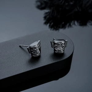 Macro detail of antique silver Sanxingdui mask earrings on a professional black display