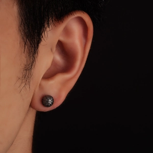 Close-up of basketball-shaped black stud earring on ear with textured metal details