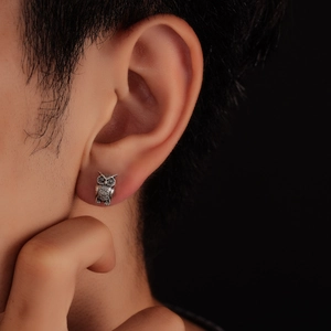 Detail of owl stud earring in vintage silver finish worn by a model on dark background