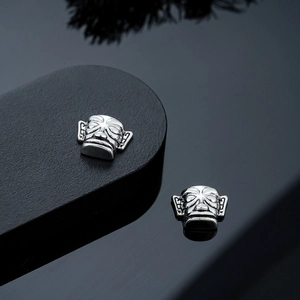 Detailed view of vintage silver Sanxingdui mask earrings on a reflective black pedestal