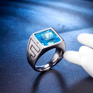 Détail d'une bague avec saphir bleu carré et anneau en métal brossé à motifs grecs