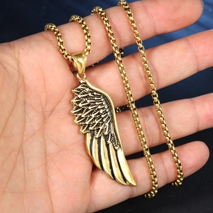Gros plan détaillé du pendentif aile dorée et de la chaîne en main sur fond sombre