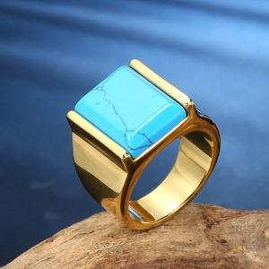 Macro shot of gold-plated square turquoise stone ring set on a natural wooden base