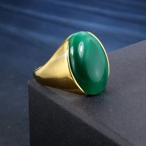 Herrenring aus goldenem Edelstahl mit großem ovalem grünem Edelstein auf dunklem Grund