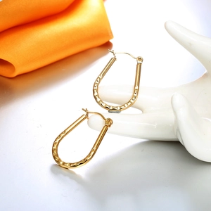 Detailed shot of gold U-shaped hoop earrings with hammered texture on white ceramic hand