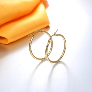 Golden stainless steel hoop earrings with textured finish on orange silk background