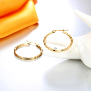 Detail of gold hoop earrings with spiral texture shown on a mannequin hand model