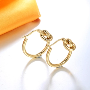 Boucles d'oreilles nœuds en acier titane plaqué or 18 carats sur une surface réfléchissante