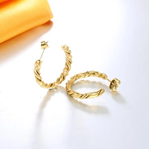 Detailed close-up of golden twisted C-shaped hoop earrings with textured spiral design