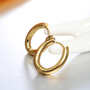 Detail view of thick gold oval hoop earrings with polished mirror finish on a model hand
