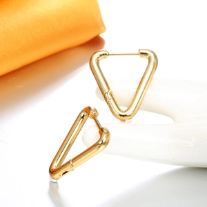 Détail de boucles d'oreilles triangles dorées sur un support main blanc, fini poli