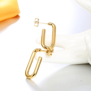 Détail macro de boucles d'oreilles dorées en U sur un support en céramique blanc