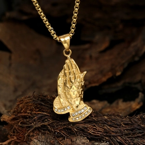 Gros plan d'un collier pendentif mains en prière dorées avec strass et détails de croix