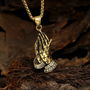 Détail du pendentif mains en prière dorées avec croix noires et cristaux sur bois