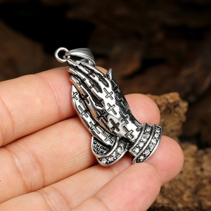 Gros plan d'un pendentif mains en prière argenté vintage avec croix en relief et zircons