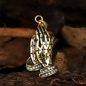 Gros plan d'un pendentif mains en prière dorées avec croix noire et strass brillants