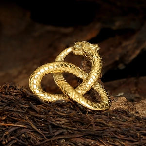 Detailed close-up of golden dual snake pendant with scales on a rustic wood background