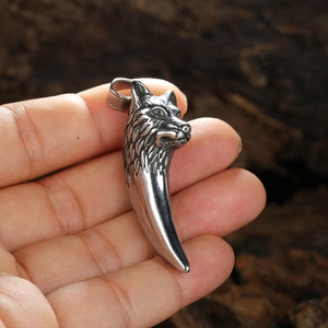 Pendentif vintage tête de loup et dent en acier inoxydable tenu à la main