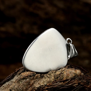 Macro shot of triangle guitar pick pendant in brushed titanium steel on wood bark