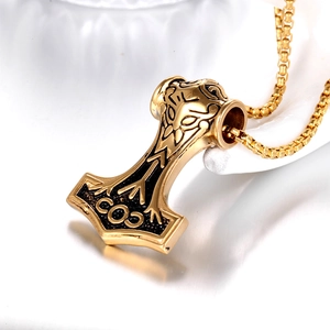 Macro detail of golden Mjölnir pendant with Nordic patterns on white ceramic base