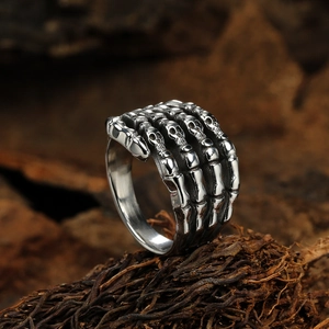 Gothic silver skull hand skeleton ring in punk rock style on a dark textured background