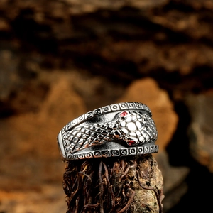 Vintage stainless steel wide snake ring with red gem eyes on a wooden bark stand