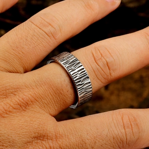 Macro view of wide silver titanium ring showing detailed bark texture on the finger