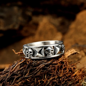 Punk style stainless steel ring featuring relief skulls and pyramid studs on a dark wood base