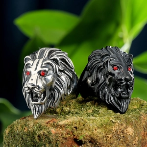 Detailed view of silver and black lion head rings with red stone eyes on a mossy rock