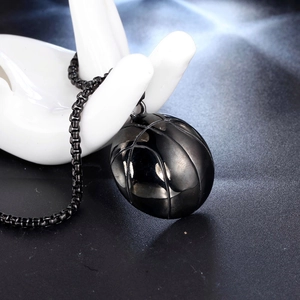 Close-up of a polished black stainless steel basketball pendant on a ceramic hand model