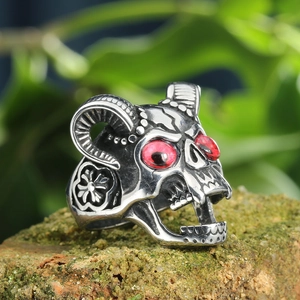 Gothic stainless steel ram skull ring with red eyes and horn texture on a mossy brick