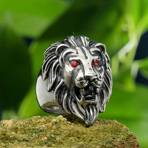 Macro shot of silver lion head ring with red gemstone eyes on a mossy stone base