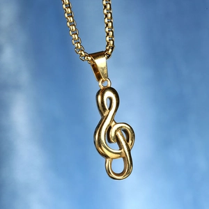 Gros plan du pendentif clé de sol doré poli avec une chaîne box sur fond bleu dégradé