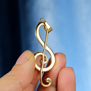 Detail of a polished gold treble clef pendant held in hand with glossy finish