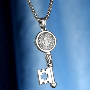 Macro shot of silver Saint Benedict key pendant with detailed box chain on blue background