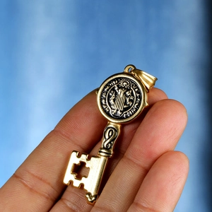 Macro shot of gold St. Benedict key pendant featuring a cross cutout and vintage details