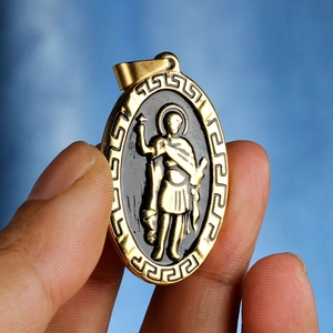 Pendentif ovale doré avec centre noir, relief de saint et bordure à clé grecque