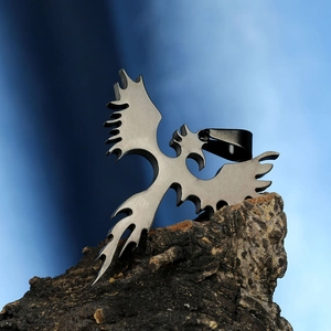 Detailed view of cutout phoenix pendant in titanium steel on natural wood texture