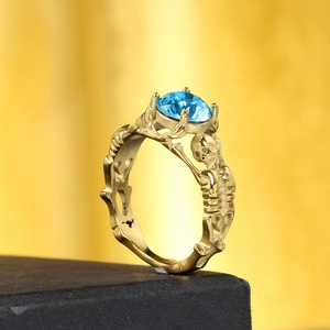Anello gotico a teschio dorato con uno zircone blu brillante di forma rotonda