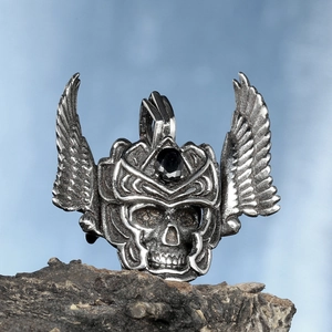 Gothic skull pendant with winged helmet and black gemstone on a rustic stone surface