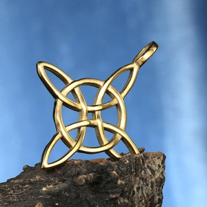 Vue détaillée d'un pendentif nœud de sorcière doré en acier inoxydable sur de l'écorce