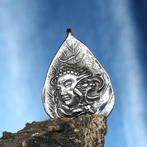 Detail of silver Buddha and skull pendant relief texture on dark volcanic rock