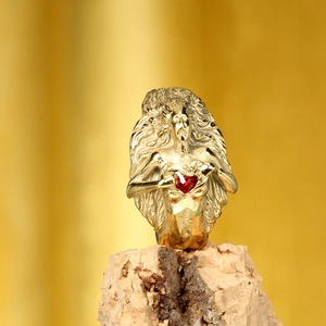 Détail d'une bague dorée avec figurine féminine gravée tenant une pierre en cœur rouge