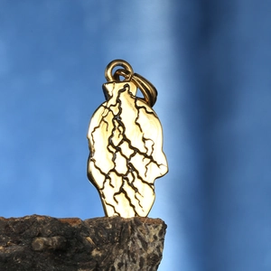 Detailed macro of gold skull pendant with black crackle finish on dark wood base