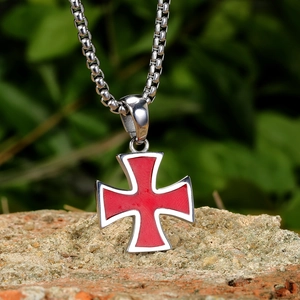 Vue détaillée du pendentif croix en acier inoxydable avec émail rouge sur fond de briques