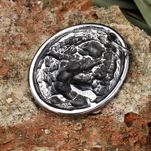 Vintage stainless steel oval flying dragon pendant with dark lava texture on a rock base